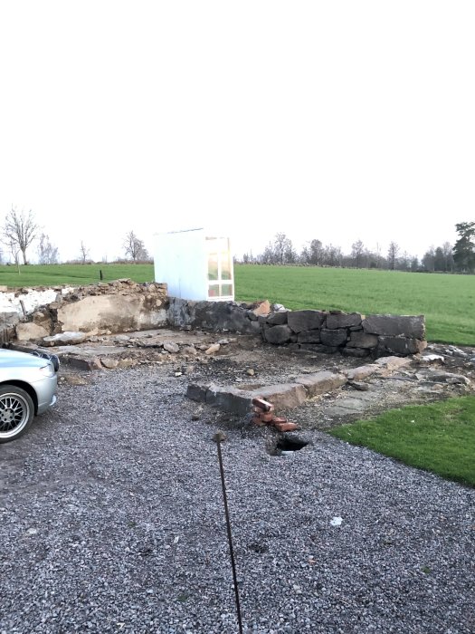 Rivningsplats med delvis rivet hus, grusmarker och en bil parkerad till vänster.