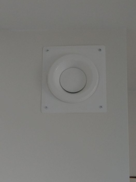 Nyinstallerad vit luftventil på en grå vägg efter ommålning och renovering.