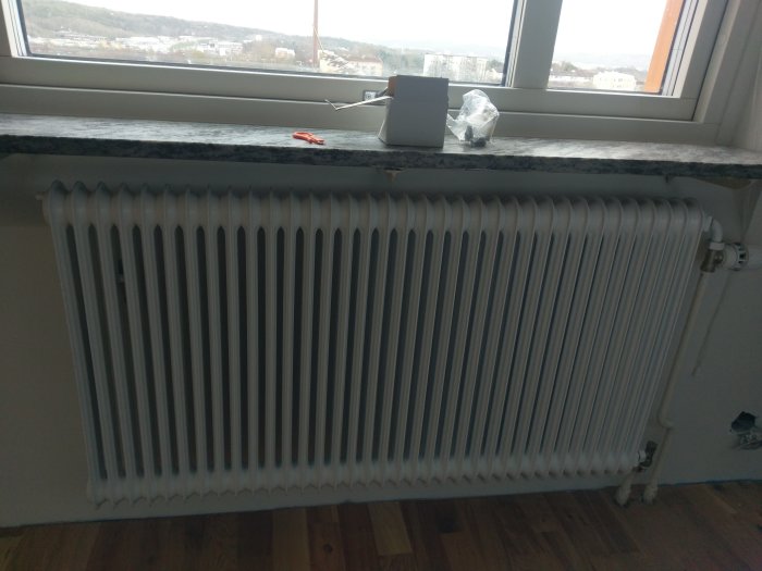 Nyrenoverad vit radiator monterad under ett fönster med nymålat fönsterbräde och parkettgolv.