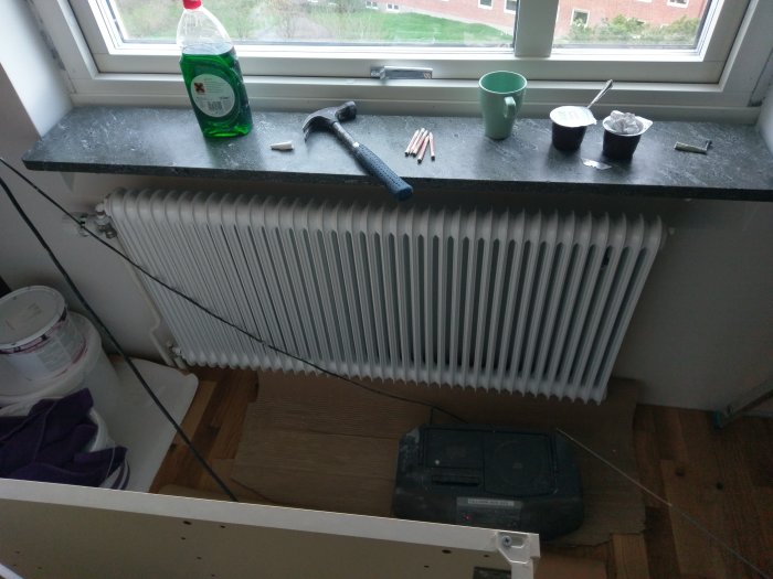 Nyinstallerat vitt element under fönster med verktyg och färgburk på fönsterbrädan i ett renoveringsprojekt.