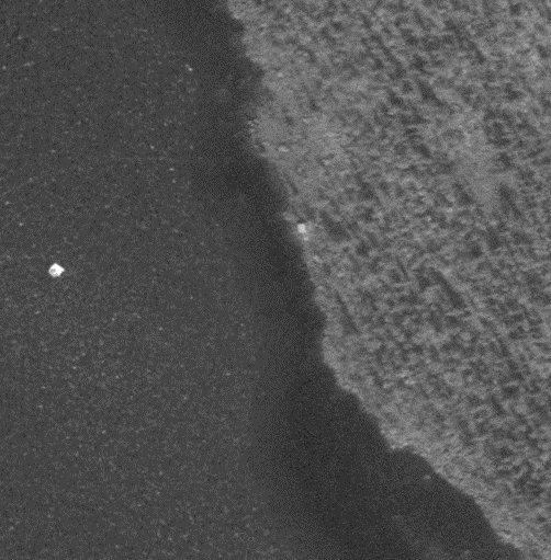 Flygfoto över sjö med potentiell byggnad eller stenblock vid strandkanten.