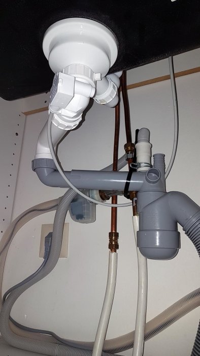 Nyinstallerad vattenlås och avloppsslang under vask, inklusive kopparledningar och elektrisk kabel.