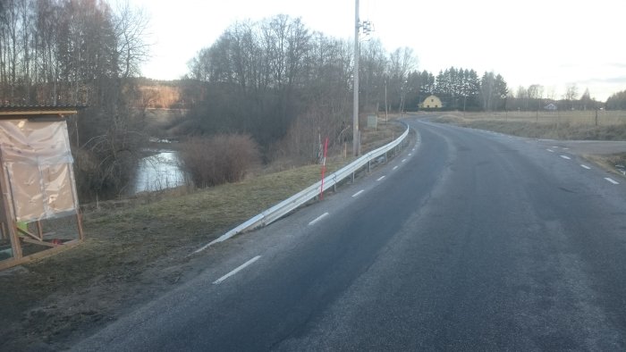 Nytt vägräcke längs kurvig landsväg hindrar åtkomst till mark, med landsbygd i bakgrunden.