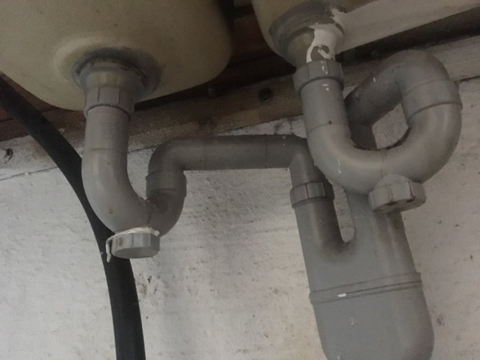 Underifrånperspektiv av ett vattenlås och avloppsrör installerade under en diskbänk.