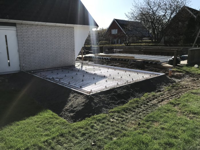 Armeringsjärn förberett för gjutning av platta vid husgrund med material på gräsmatta.