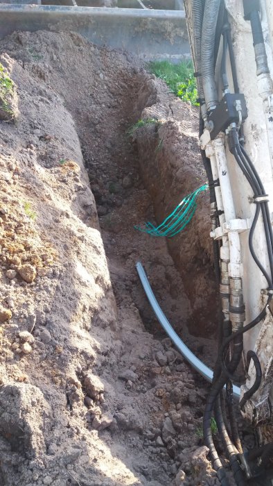 Nygrävd grävning med synlig fiberkabel under jorden bredvid en maskins hydraulslangar.