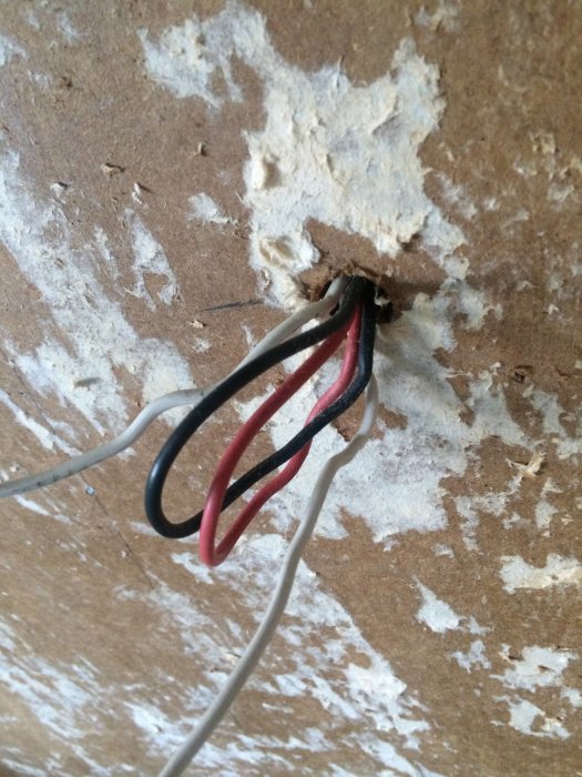 Tre exponerade elektriska kablar i svart, rött och vitt som sticker ut från ett hål i väggen.