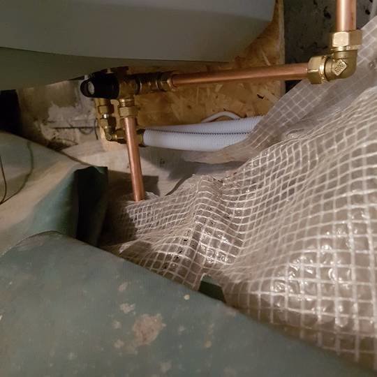 Varmvattenberedare med rör och trycktank monterade i torpargrunden under ett hus.