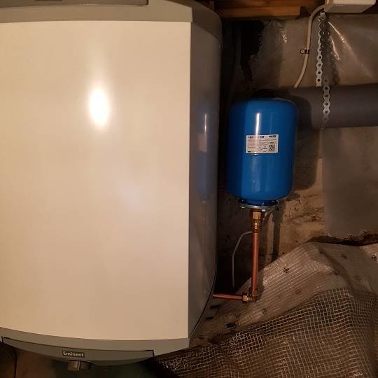 Varmvattenberedare och en blå trycktank installerade i en torpargrund under ett hus.