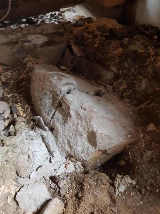 Stor sten som delvis grävts fram under husrenovering med grus och jord omkring.