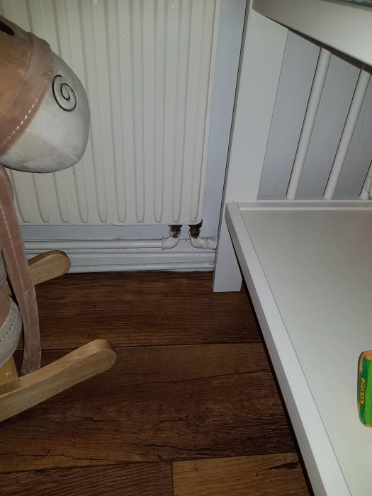 Radiator med synliga rör för potentiellt enrörsystem, nära golv och möbler under renovering.