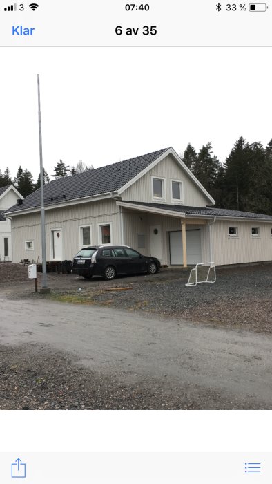 Ett vitt hus med svart tak, temporär trappa och en parkerad bil framför, i ett område under konstruktion.