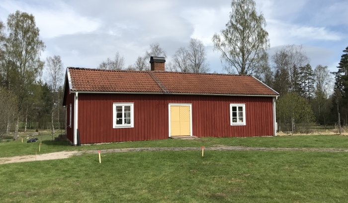Rött torp med nygjord dörr i gammal stil, beige med vita kanter, traditionellt svenskt ladhus.