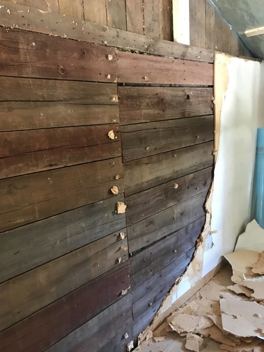 Delvis rivna väggbeklädnader visar gammal, sliten träpanel utan synliga reglar i en äldre bostad under renovering.