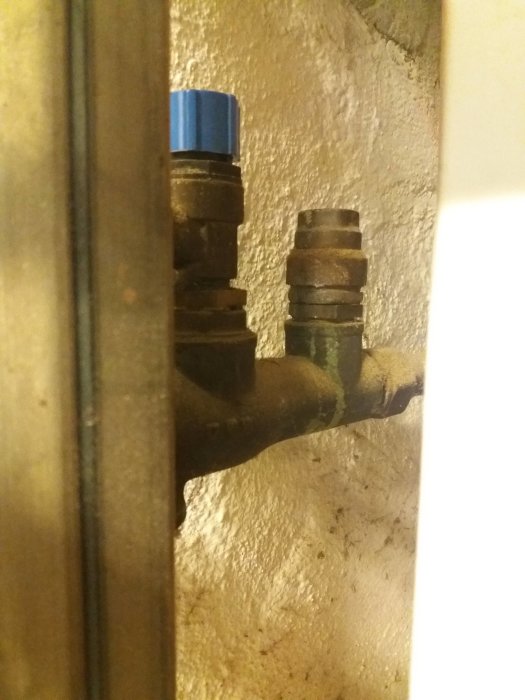 En närbild av en gammal och använd röranslutning med en blå kork, eventuellt en säkerhetsventil, i ett värmeinstallationssystem.