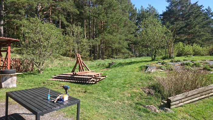 Solig trädgård efter rivet staket med stabila stolpar på marken, verktyg på bord och naturskön bakgrund.