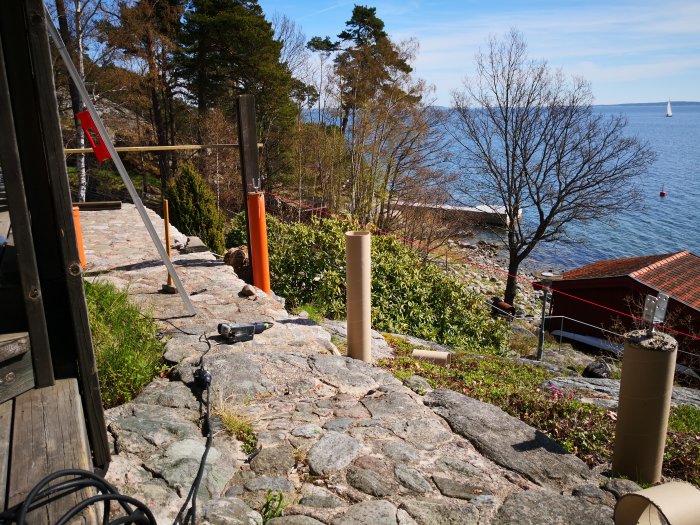 Byggplats utomhus med pågående utvidgning av veranda, verktyg synliga, med utsikt över havet och segelbåt.