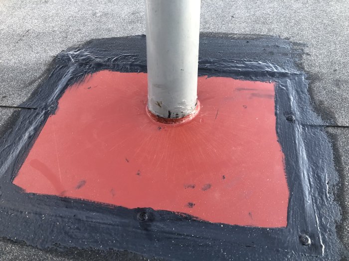 Genomföring av skorstensrör med rött underbeslag på svart takmaterial, enligt AMA-figur.