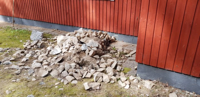 Hög med utgrävda stenar nära husvägg och rabatt vid en renovering.