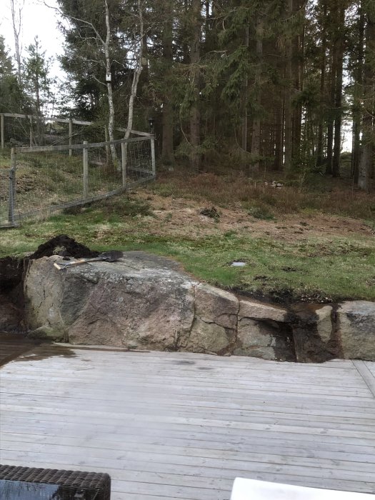 Jord och gräs hänger över bergskanten intill en träaltan, potentiellt skapande gyttjeproblem vid regn.