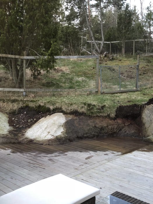 Altan med överhängande jord och gräs nära bergskant intill trätrall.
