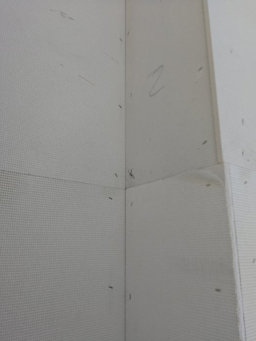 Närgränsad bild på putsskivor monterade på en vägg, med synliga kryssskarvar och fastkortsklips mindre än 10 mm från skivkanten.