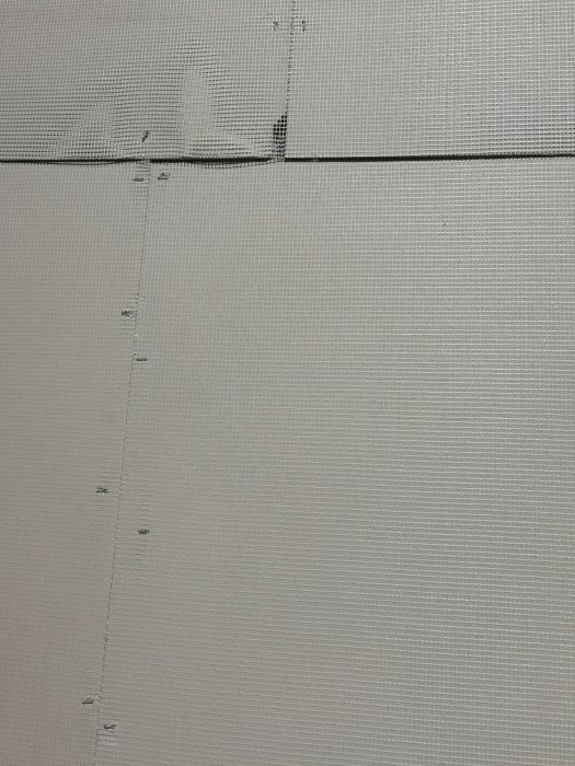Putsskivor monterade på trästomme med synliga kryssskarvar och ojämnt placerade fästklamrar.