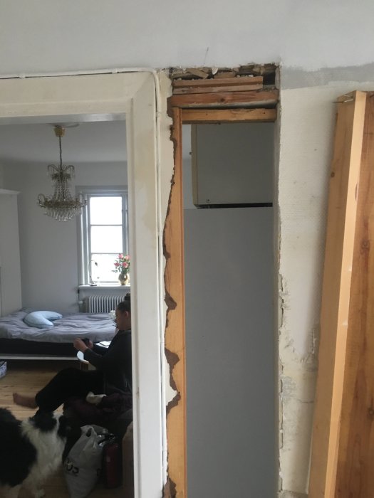 Renoveringsarbete av en dörröppning i ett hem med synlig trästomme och en person i bakgrunden.