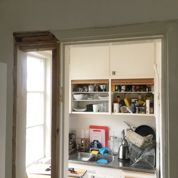 Vy genom dörröppning mot ett kök under renovering med synliga tegel och inredningsdetaljer.