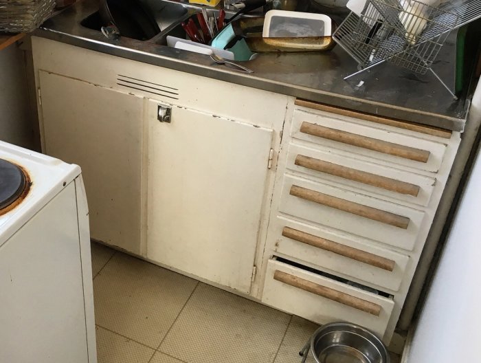 Gamla vitvaror och skåp i ett slitet kök i behov av renovering.