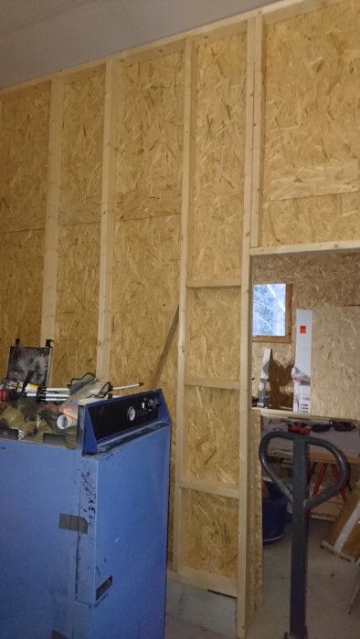 Inomhusbyggarbetsplats med OSB-paneler på väggar och olika verktyg och byggmaterial.