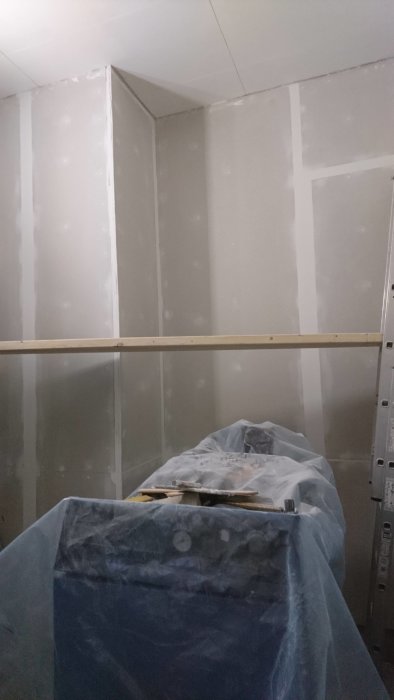 Renoveringsrum med osatt klinker och spacklade gipsskivor, skyddad byggmaterial under plast.