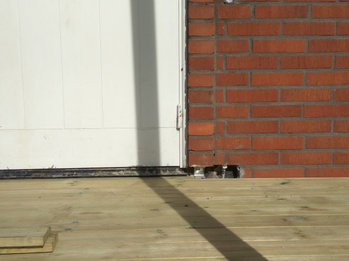 Nybyggd träveranda som möter en vit vägg och en röd tegelmur, där en gammal stentrappa tagits bort.