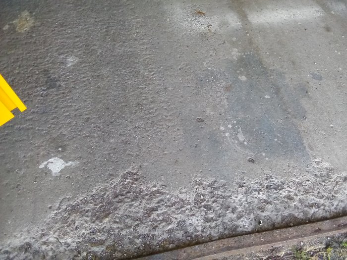 Slitet betonggolv i garage med fläckar och skador som behöver repareras.