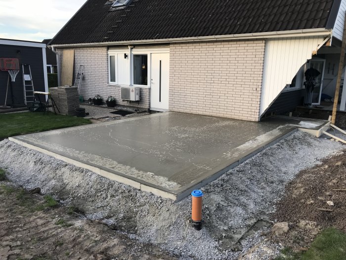 Nyligen gjuten betongplatta med vattenspegel bredvid ett bostadshus, provmätt golvvärmekablage synligt.