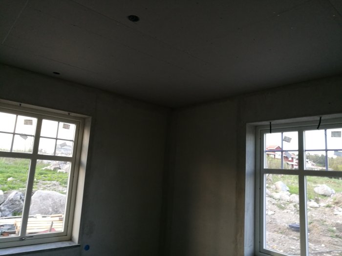 Inomhusvy av ett hörnrum under renovering med OSB och gips i taket samt nyligen putsade väggar.