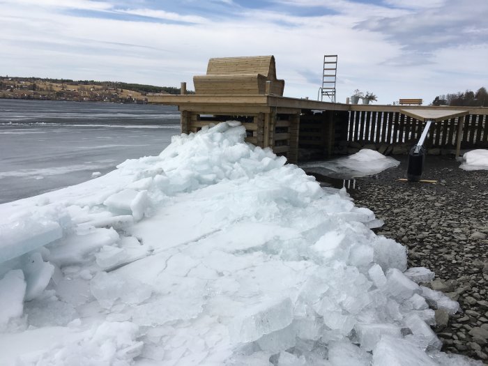 Isblock som trängt upp mot en brygga vid sjö med isbelagd yta i bakgrunden.