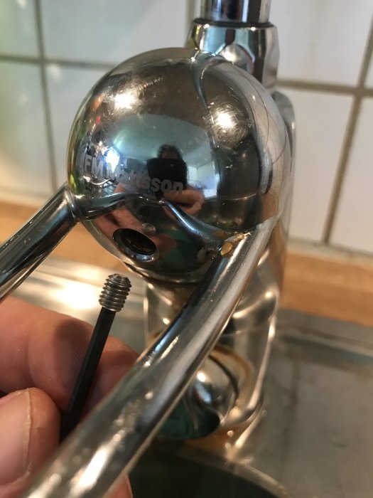 Närbild av en köksblandare med en demonterad insektsskruv i handen, med fokus på delen där handtaget sitter fast.