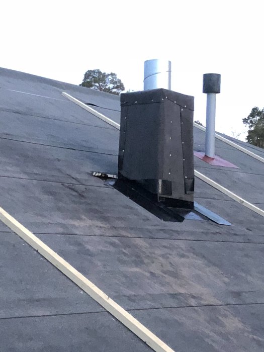 Nybyggd trälåda med papp och underbeslag för köksfläkt på ett tak vid skymning.