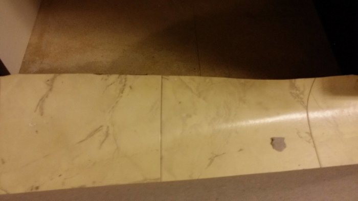 Upprullad plastmatta med möjlig vattenskada och synliga slitage, misstänkt för asbest, från ett äldre hus.