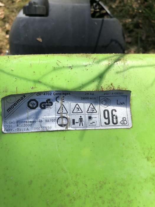 Identifieringsskylt på gräsklippare med tekniska data och säkerhetsvarningar.