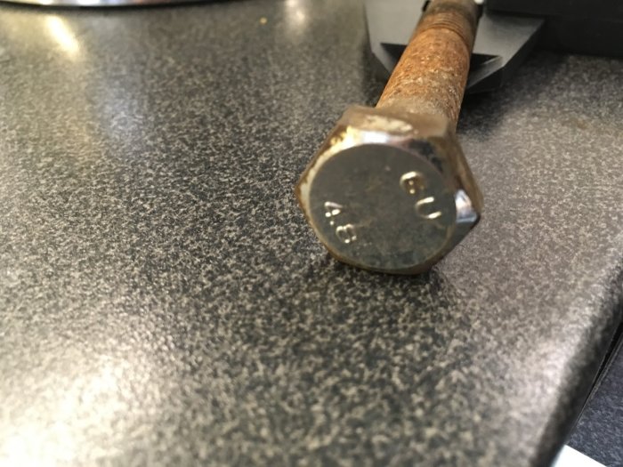 Närbild av en rostig sexkantskruv med märkningen "GU 4,8" på en grå yta.