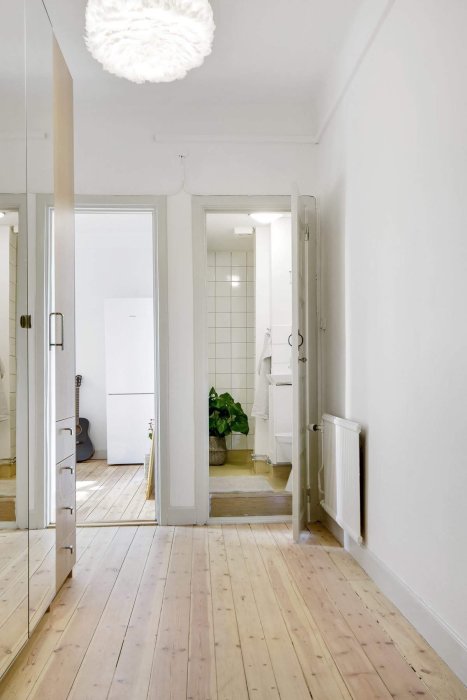 Nyrenoverad lägenhetskörridor med ljusa väggar, trägolv och öppen dörr till badrummet.
