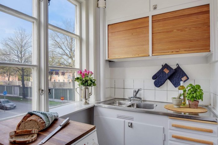 Renoverat kök med vita skåp och träpanel, inredningsdetaljer och utsikt genom fönstret.