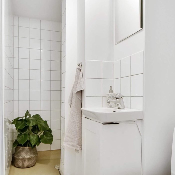 Renoverat badrum med vita kakelväggar, handfat, spegel och grön växt i korg.