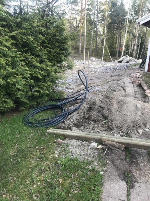 Vattenledningsslang ligger ovanpå grävd mark nära ett hus med trädgård i bakgrunden.