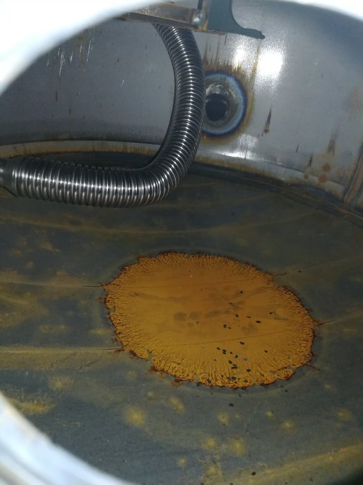 Insidan av en ny ackumulatortank med synliga anslutningar och en rostliknande fläck på botten.