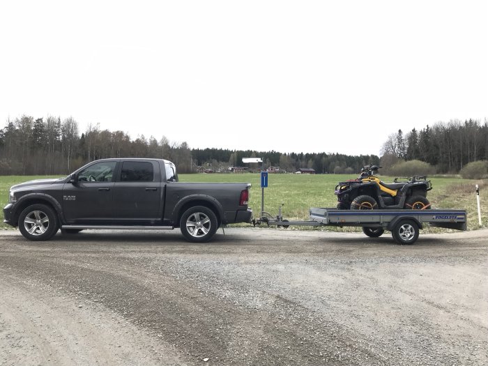 Pickupbil med en Thule/Fogelsta släpvagn lastad med en gul fyrhjuling parkerad på en grusväg.