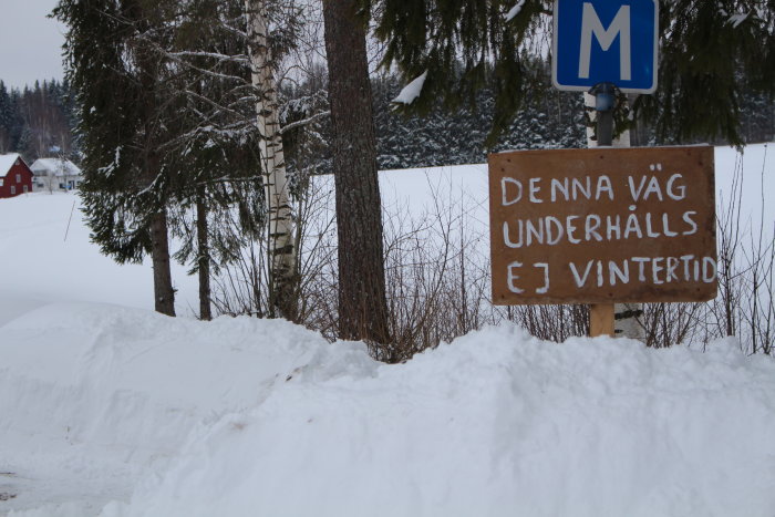 Skylt i snölandskap med texten "DENNA VÄG UNDERHÅLLS EJ VINTERTID" bredvid en vägmärkning.