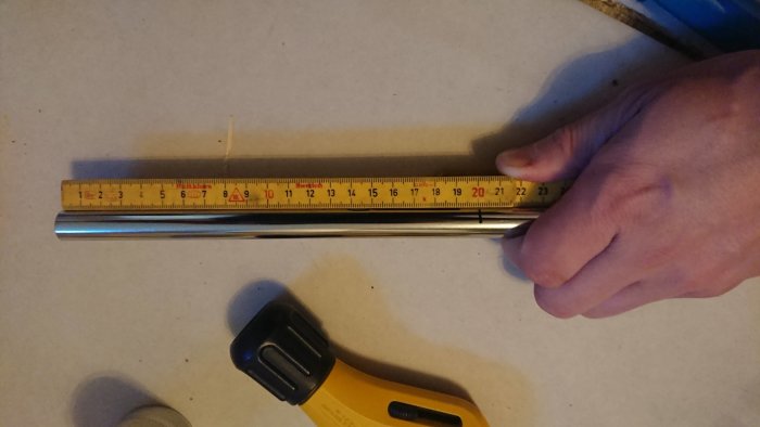 Hand mäter kromat 15mm rör med tumstock, rörskärare och avgradare synliga.